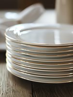 Stack of clean white porcelain dinner plates on rustic wooden table surface with soft natural lighting, creating elegant dining atmosphere for food photography.