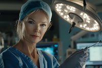 Female surgeon in operating room wearing surgical cap, mask, and gloves, standing beneath overhead surgical lights. Professional healthcare setting for medical, hospital, and surgical training content.