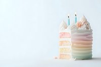 Pastel rainbow layered birthday cake with whipped cream frosting and blue candles on white background, slice reveals moist vanilla interior layers.