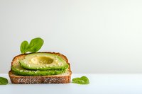 Whole grain bread slice topped with creamy avocado spread and fresh basil leaves on white surface. Healthy breakfast or lunch sandwich ingredient for food styling and culinary projects.
