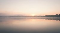 Serene dawn landscape with calm lake reflecting soft pastel sky, misty atmosphere, and distant treeline. Peaceful nature scene for meditation, wellness, and relaxation projects.