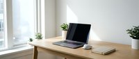 Modern minimalist home office workspace with laptop computer on wooden desk near bright window with natural light and green plants for productivity.