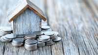Small wooden house model surrounded by silver coins on rustic wood surface representing real estate investment, mortgage savings, property finance concept.