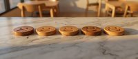 Five wooden emoji face tokens arranged on marble surface showing different emotions from sad to happy in warm cafe setting.