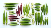 Okra pods in various sizes and stages of ripeness arranged flat lay with sliced cross sections on white background, suitable for food photography, culinary blogs, recipe illustrations, and healthy eating content.