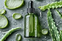 Green glass dropper bottle with aloe vera extract surrounded by fresh cut aloe leaves and lime slices on wet gray surface with water drops, natural skincare concept.