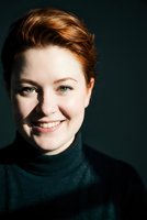 Young Caucasian woman with short auburn hair smiling warmly in dark green turtleneck sweater against black background for portrait photography.