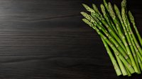 Fresh green asparagus spears arranged on dark wooden background with copy space, raw organic vegetables for healthy cooking and food photography.