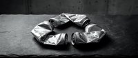 Crumpled metallic foil packets arranged in circle on dark concrete surface, suitable for packaging design and product mockups.