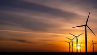 Wind turbines silhouetted against dramatic sunset sky with orange and purple clouds, renewable energy concept for sustainable power generation.