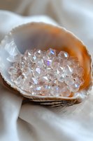 Iridescent crystals nestled in seashell on white silk fabric, creating magical sparkle effect with rainbow reflections and natural organic composition.