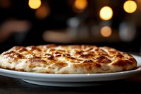 Golden braided bread loaf with glossy crust on white plate against warm bokeh lights background for bakery and food photography.