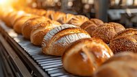 Fresh baked bread rolls and buns with various toppings arranged in row on cooling rack, golden crust and sesame seeds, warm morning bakery atmosphere.