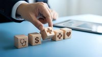Healthcare professional arranging wooden blocks with medical and financial symbols, representing integration of health services, insurance coverage, and wellness planning on office desk.