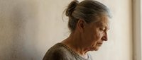 Senior woman with gray hair in bun, wearing knit sweater, looking thoughtfully to side in natural light. Suitable for aging, wellness, contemplation themes.