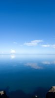 Serene calm ocean water with clear blue sky and white clouds reflecting on glassy surface, ideal for travel and nature backgrounds.