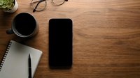 Modern workspace flat lay with smartphone, coffee cup, notebook and glasses on wooden desk background for business and productivity concepts.