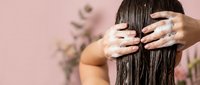 Woman applying hair treatment mask to long brunette hair in spa setting with hands massaging scalp for healthy haircare routine and beauty wellness.