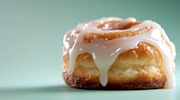 Sweet glazed cinnamon roll with creamy white vanilla icing dripping down sides against mint green background, macro food photography showing texture details.
