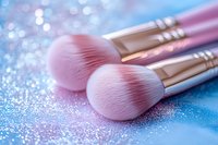 Pink makeup brushes with soft bristles on sparkly blue glitter background in dreamy pastel colors, professional cosmetic tools for beauty application.