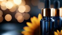 Dark glass dropper bottle with essential oil against blurred bokeh lights and sunflower petals, wellness and aromatherapy concept for spa and natural cosmetics.