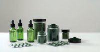 Green glass bottles with droppers, jars and white pills arranged on clean surface for pharmaceutical and wellness product packaging design.