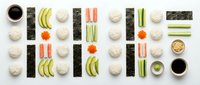 Sushi making ingredients arranged in organized grid pattern with nori sheets, rice, avocado, cucumber, salmon and wasabi on white background.