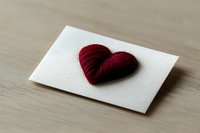 Red embroidered heart on white textured paper card placed on wooden surface for romantic greeting cards and craft projects.