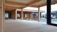 Modern wooden building interior with exposed timber beams, natural pine flooring, and large windows showing construction phase of sustainable architecture project.