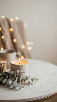 Cozy home interior with burning candle, eucalyptus branches and warm fairy lights creating peaceful hygge atmosphere for relaxation and mindfulness.