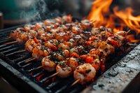 Grilled shrimp skewers with herbs and spices cooking on flaming barbecue grill, close-up view of seafood kebabs with charred marks and orange flames.