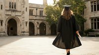 Young woman graduate in black cap and gown walking across university courtyard after commencement ceremony celebrating academic achievement and educational milestone.