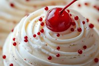 Creamy white frosting swirl topped with maraschino cherry and red sugar pearls in macro view, sweet dessert decoration detail for cakes and cupcakes.