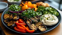 Grilled vegetables and hummus platter with charred eggplant, colorful bell peppers, fresh herbs and creamy dip served on dark plate. Mediterranean appetizer.