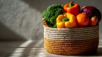 Fresh vegetables in woven basket with dramatic lighting, featuring colorful bell peppers, broccoli and red onion for healthy eating and food photography.