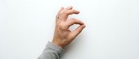 Male hand with light skin tone wearing gray sleeve making pinching gesture against white background, isolated for design use on marketing materials, websites, and presentations.