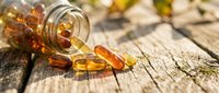 Amber vitamin capsules spilling from glass bottle onto rustic wooden surface for health and wellness supplement marketing materials.