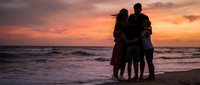 Family silhouette embracing on beach at sunset with orange sky and ocean waves. Parents with children enjoying peaceful moment during golden hour vacation.