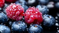Fresh ripe raspberries and blueberries with water drops in macro shot. Natural organic berries with morning dew closeup on dark background.