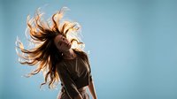 Young woman with flowing brown hair dancing against blue sky background, expressing freedom and joy in motion.