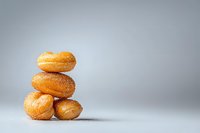Fresh sugar-coated mini donuts stacked in creative composition on light gray background with soft shadows and copy space for bakery marketing.