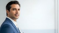 Professional businessman in blue suit looking confident in modern office environment with natural lighting and clean minimalist background.