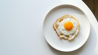 Fresh fried egg with golden yolk on white plate, top view breakfast meal ready to eat on clean table surface for cooking and food photography.