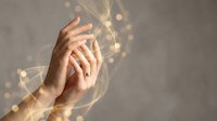 Elegant female hands with gold ring surrounded by glowing bokeh light waves on gray background, symbolizing luxury and romance.