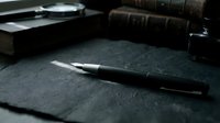 Elegant fountain pen resting on dark textured paper beside vintage books, magnifying glass, and ink bottle in moody, dramatic lighting.