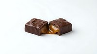 Chocolate candy with caramel filling, broken in half to show interior, isolated on white background for confectionery packaging and food advertising.