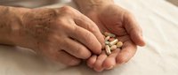 Senior adult hands holding handful of white and beige pills and capsules on marble surface for healthcare, medicine, and pharmaceutical concepts.