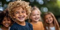Diverse group of happy children laughing outdoors with natural bokeh background. Curly blonde boy in navy shirt leads playful moment with multicultural friends.