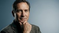 Middle-aged Caucasian male professional in thoughtful pose, hand to chin, wearing olive green sweater against blue gradient background. Corporate portrait.