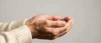 Elderly person's cupped hands in receiving gesture wearing cream knit sweater against neutral background showing aging skin texture and life experience.